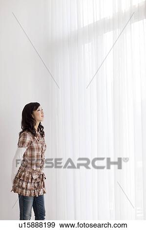 Young woman standing by window View Large Photo Image Stock Photo - Young woman standing by window. Fotosearch