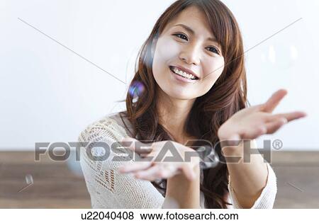 Young woman trying to catch soap bubbles, smiling View Large Photo Image Stock Photo - Young woman trying to catch soap bubbles, smiling. Fotosearch