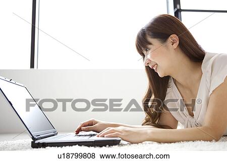Stock Photo - Young woman using laptop, lying on rug. Fotosearch
