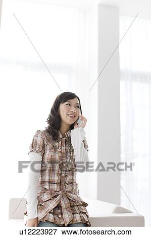 Stock Photo - Young woman using mobile phone, smiling. Fotosearch
