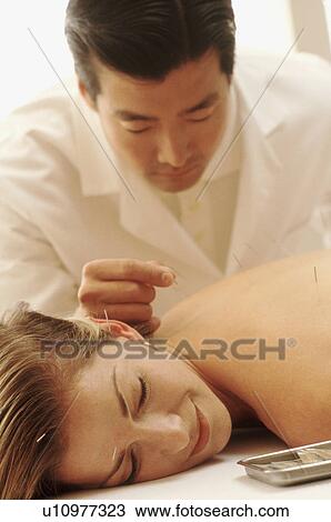 Stock Image - Acupuncturist putting needles in woman's back. Fotosearch