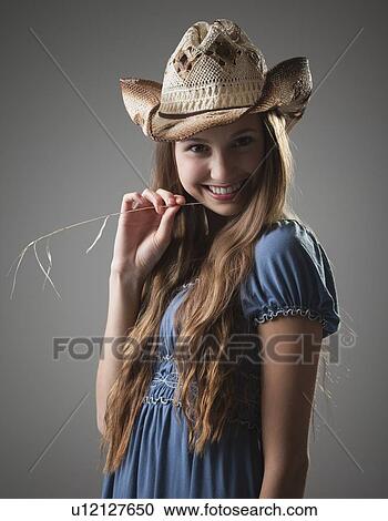 Stock Image - Beautiful long haired cowgirl chewing on grass. Fotosearch
