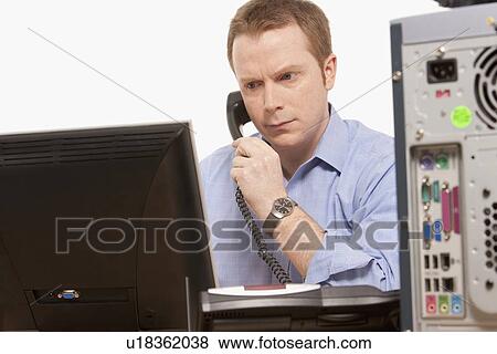 Stock Photo - Businessman talking on phone while looking at computer. Fotosearch
