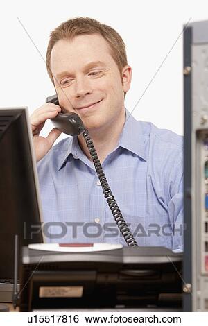 Stock Photograph - Businessman talking on phone while looking at computer. Fotosearch