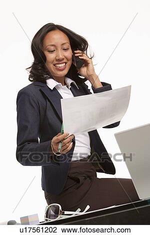 Stock Image - Businesswoman sitting on desk. Fotosearch