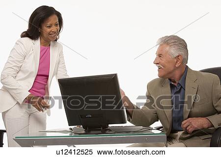 Stock Photography - Colleagues talking while looking at computer. Fotosearch