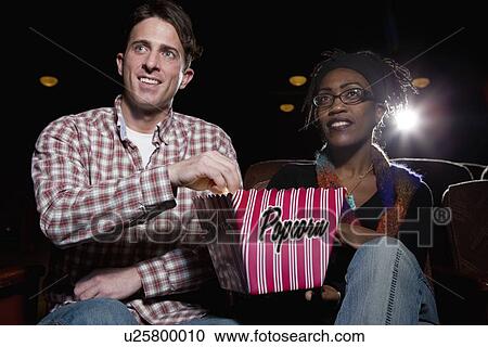 Stock Image - Couple eating popcorn in movie theatre. Fotosearch