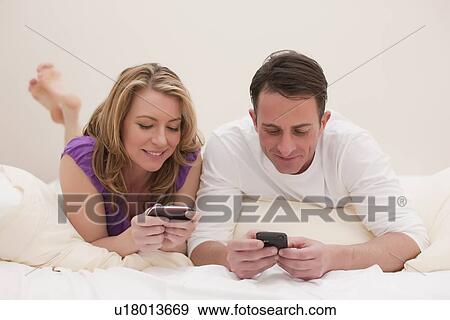 Couple lying on bed while texting View Large Photo Image Stock Photo - Couple lying on bed while texting. Fotosearch