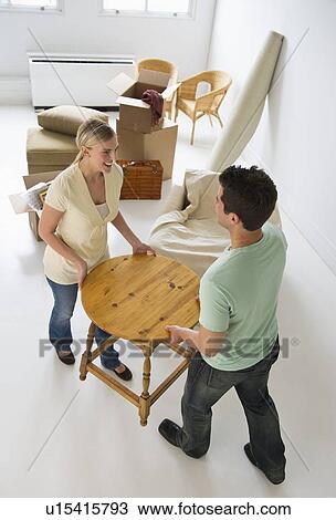 Stock Image - Couple moving furniture in their new home. Fotosearch