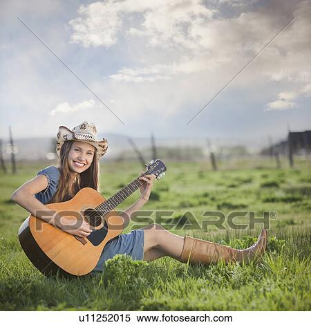 Stock Photography - Cowgirl sitting in field playing guitar. Fotosearch