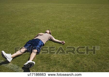 Stock Image - Defeated athlete lying on grass. Fotosearch