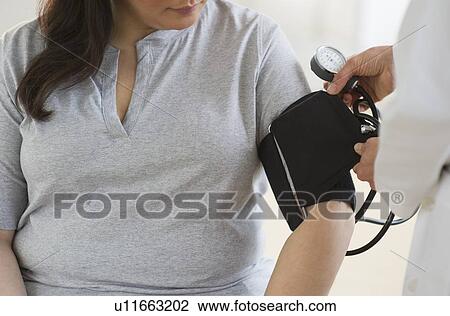 Stock Image - Doctor checking woman's blood pressure. Fotosearch