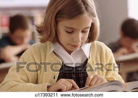 Stock Image - Elementary school student reading book at her desk. Fotosearch