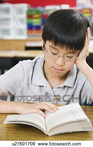 Stock Photo - Elementary school student reading book at desk. Fotosearch