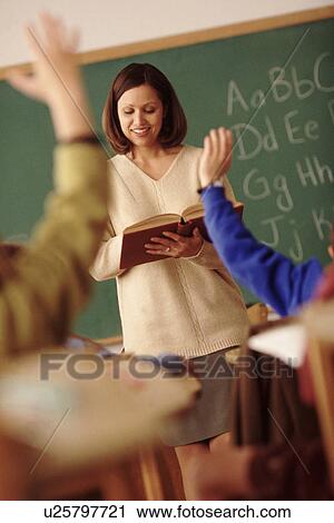 Stock Image - Elementary school students raising their hands in class. Fotosearch