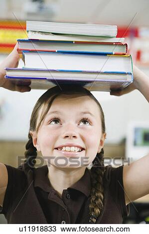 Stock Image - Elementary student holding a stack of books on her head. Fotosearch