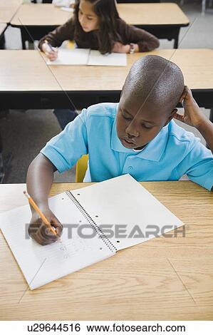 Stock Photograph - Elementary students writing in notebooks at their desks. Fotosearch