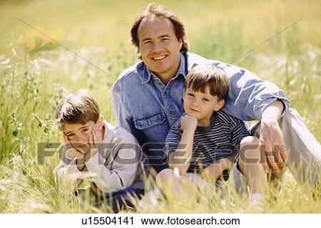 Stock Image - Father and his two sons sitting in meadow together. Fotosearch