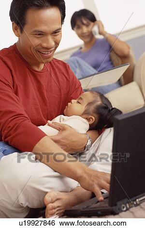Father holding his sleeping daughter while typing View Large Photo Image Stock Photograph - Father holding his sleeping daughter while typing. Fotosearch