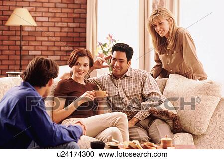 Stock Image - Four friends socializing in living room. Fotosearch