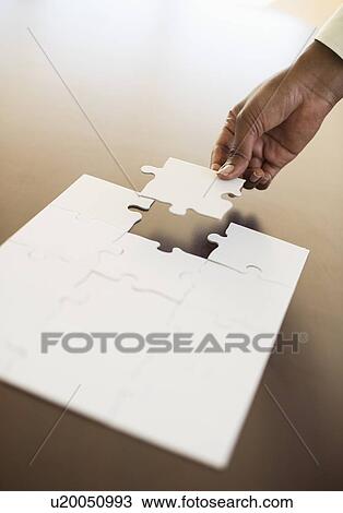Stock Image - Hand putting last puzzle piece in puzzle. Fotosearch
