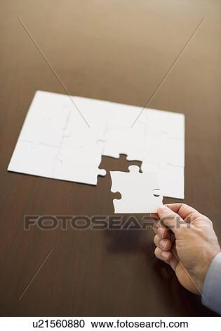 Stock Image - Hand putting last puzzle piece in puzzle. Fotosearch