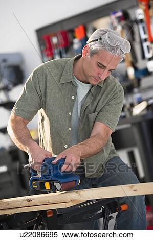 Stock Photography - Handyman sanding a piece of wood in workshop. Fotosearch