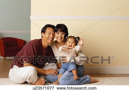 Stock Photo - Happy parents sitting on the floor with their infant daughter. Fotosearch