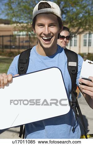 Stock Photography - Happy teenage student holding blank whiteboard. Fotosearch