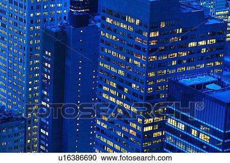 Stock Image - Illuminated buildings in New York City at sunset. Fotosearch