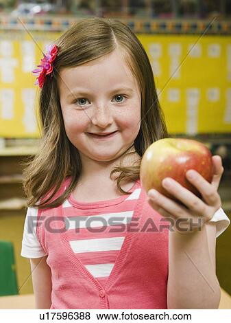 Stock Photo - Kindergarten student holding an apple in classroom. Fotosearch