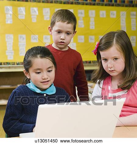 Stock Image - Kindergarten students looking at laptop in classroom. Fotosearch