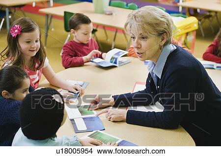 Picture - Kindergarten students sitting at table with teacher. Fotosearch