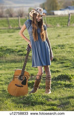 Stock Image - Long haired cowgirl holding guitar in field. Fotosearch