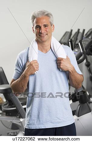 Stock Image - Man at the gym standing with towel around his neck. Fotosearch