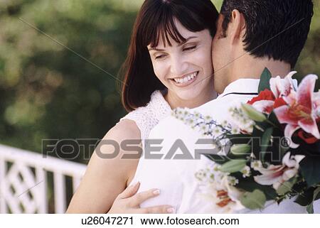Stock Image - Man kissing woman as he holds flowers behind his back. Fotosearch