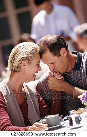 Stock Image - Man kissing woman's hand while sitting at patio table. Fotosearch
