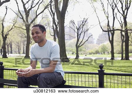Stock Image - Man sitting on bench in Central Park. Fotosearch