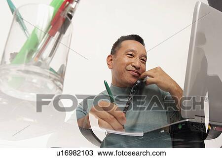 Man talking on phone while working on laptop View Large Photo Image Stock Image - Man talking on phone while working on laptop. Fotosearch