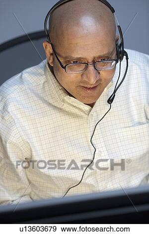 Stock Photo - Man wearing headset working on computer. Fotosearch