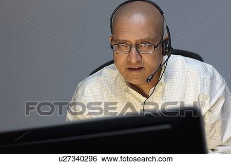 Man wearing headset working on computer View Large Photo Image Stock Photograph - Man wearing headset working on computer. Fotosearch