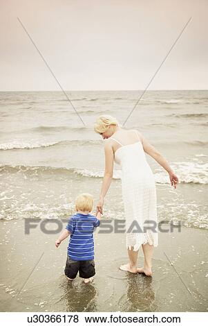 Mother and child walking hand in hand at the water's edge View Large Photo Image Stock Photo - Mother and child walking hand in hand at the water's edge. Fotosearch