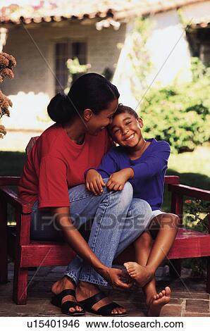Stock Photograph - Mother and daughter sitting on bench in garden. Fotosearch