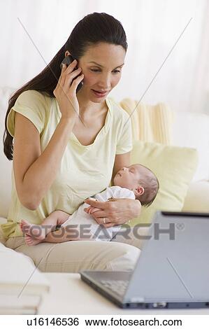 Stock Photograph - Mother talking on phone while holding her baby. Fotosearch
