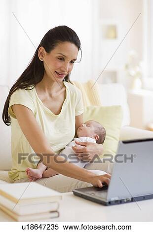 Stock Photography - Mother typing while holding baby. Fotosearch