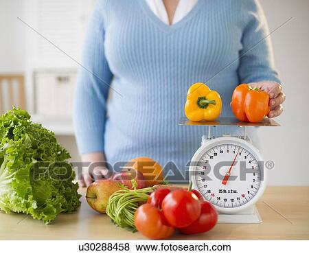 Overweight woman measuring peppers on a food scale View Large Photo Image Stock Photo - Overweight woman measuring peppers on a food scale. Fotosearch