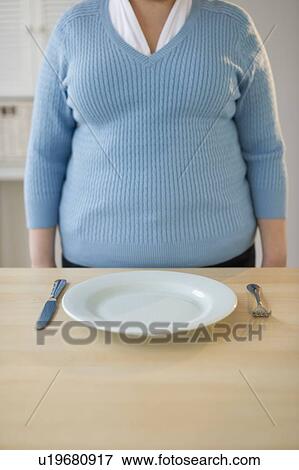 Stock Photo - Overweight woman standing in front of place setting. Fotosearch