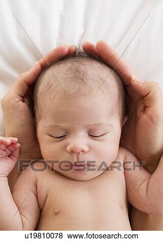 Stock Photo - Parent's hands wrapped around sleeping baby's head. Fotosearch