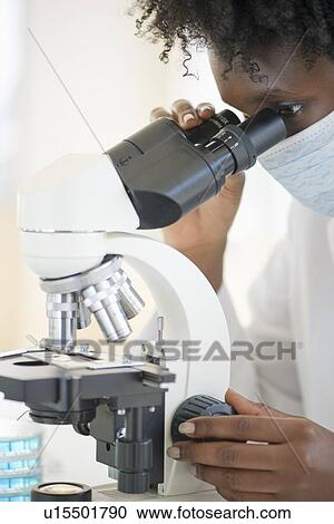 Stock Image - Researcher looking at specimen through microscope. Fotosearch