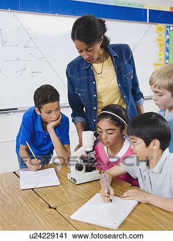 Stock Image - Teacher and elementary students looking at microscope. Fotosearch